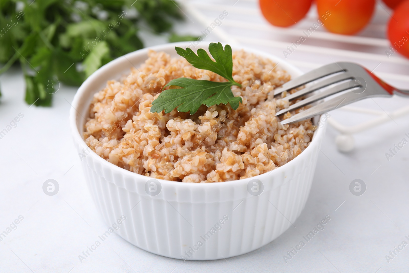 Photo of Tasty wheat porridge with parsley in bowl on white table, closeup