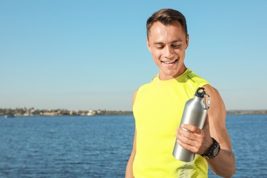 Photo of Young sporty man with water bottle outdoors on sunny day. Space for text