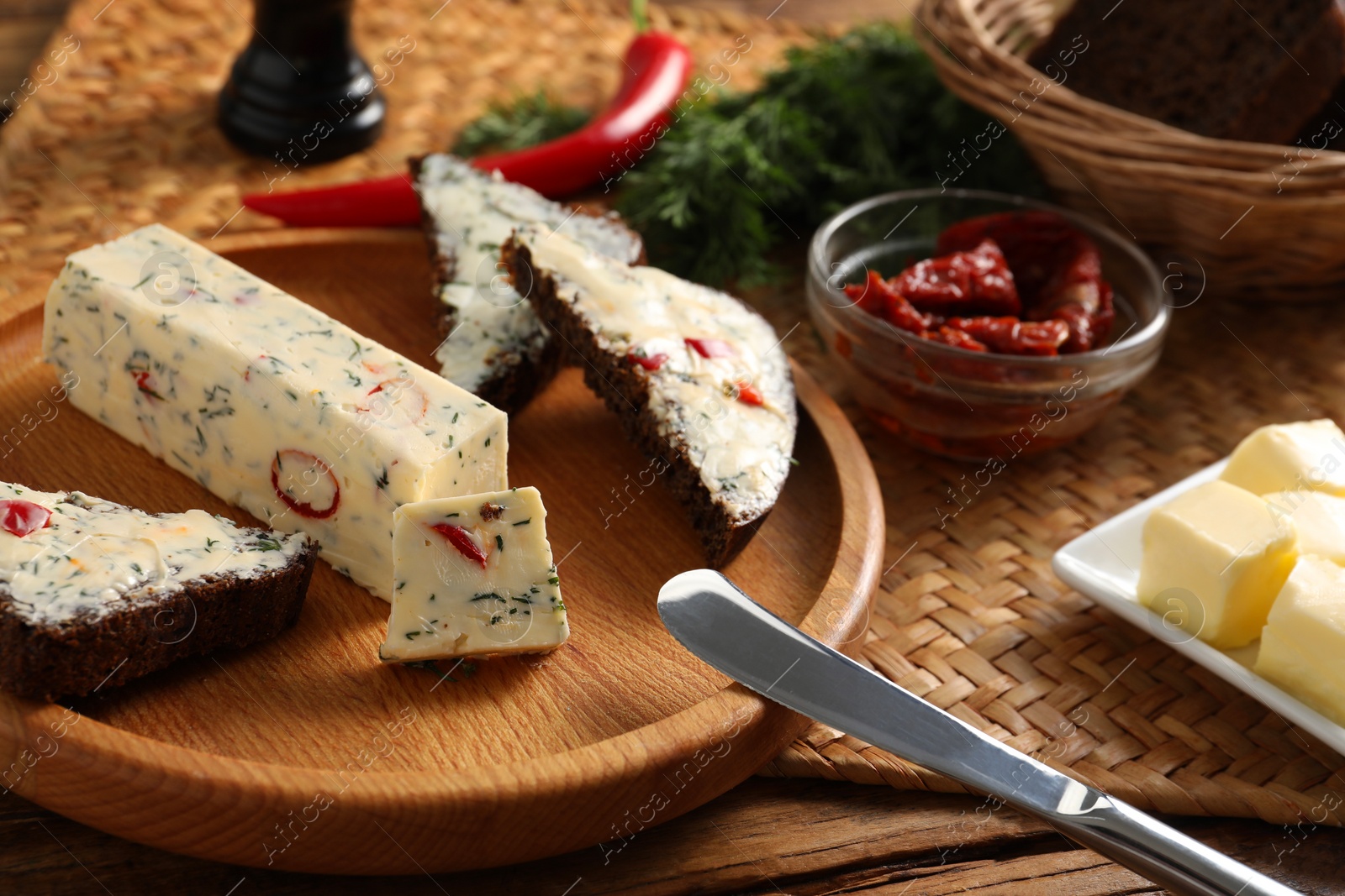 Photo of Tasty butter, dill, chili peppers and rye bread on wooden table