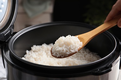 Woman taking tasty rice with spoon from cooker in kitchen, closeup