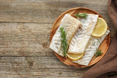 Photo of Fresh raw cod fillets with rosemary and lemon on wooden table, flat lay. Space for text