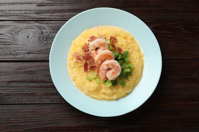 Photo of Plate with fresh tasty shrimps, bacon and grits on dark wooden table, top view