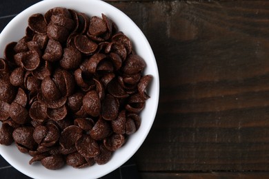 Photo of Breakfast cereal. Chocolate corn flakes in bowl on wooden table, top view. Space for text