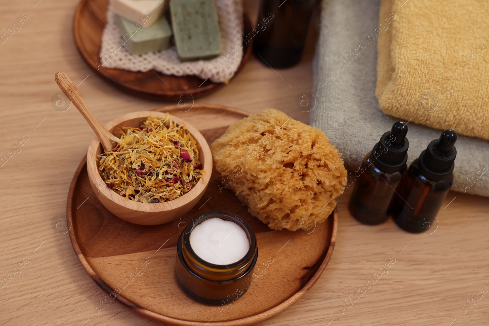 Photo of Dry flowers, bottles of essential oils, loofah and jar with cream on wooden table. Spa time