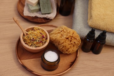 Photo of Dry flowers, bottles of essential oils, loofah and jar with cream on wooden table. Spa time