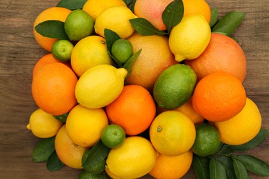 Photo of Different citrus fruits with green leaves on wooden table, flat lay