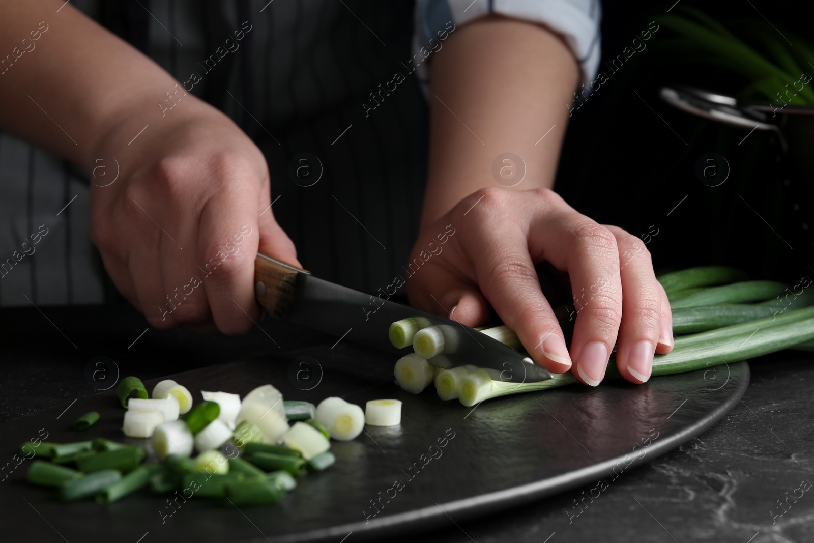 Photo of Woman cutting green spring onions at black table, closeup