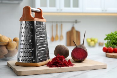 Photo of Grater and fresh ripe beetroots on white table in kitchen