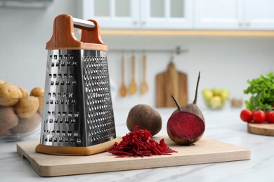 Grater and fresh ripe beetroots on white table in kitchen