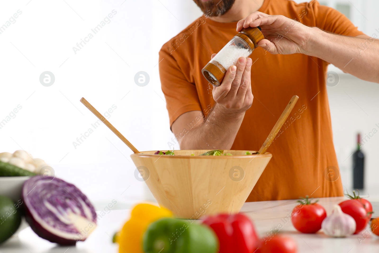 Photo of Man salting salad at table in kitchen, closeup. Online cooking course