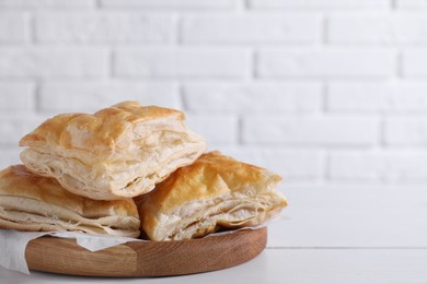 Delicious puff pastry on white wooden table against brick wall, space for text