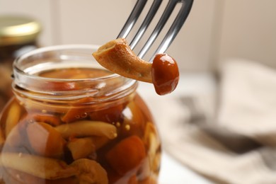 Photo of Fork with delicious marinated mushroom and glass jar on table, closeup