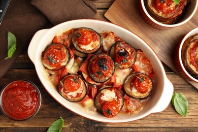 Baked eggplant with tomatoes, cheese and basil served on wooden table, flat lay