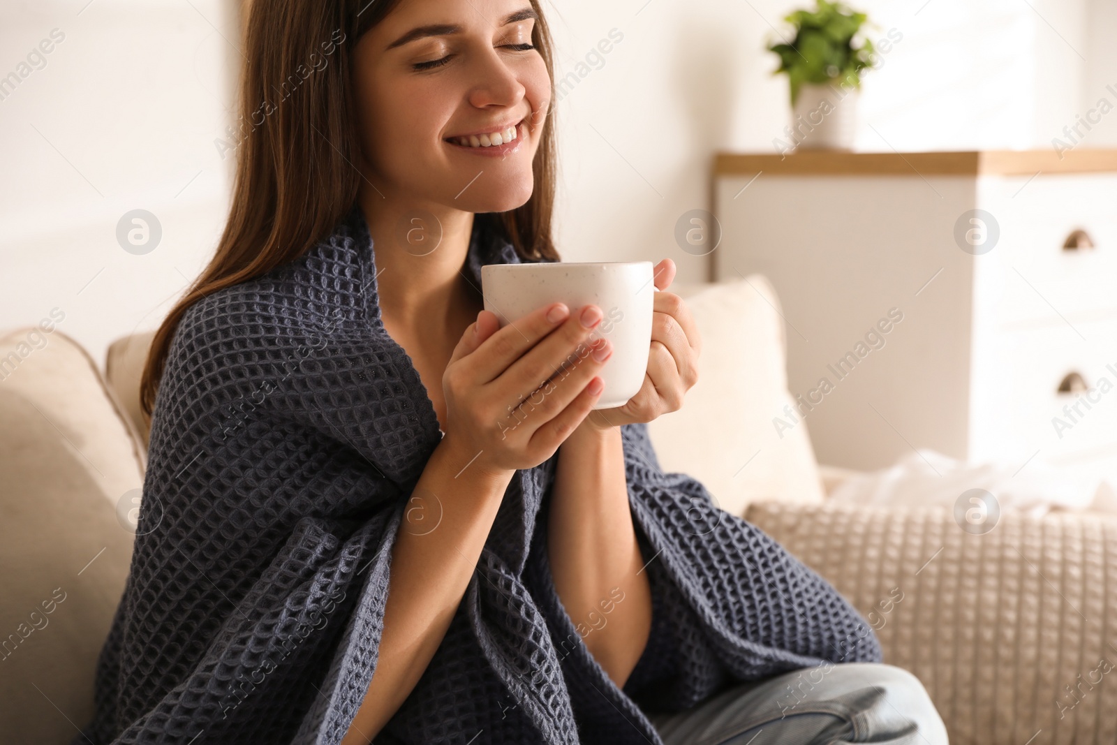 Photo of Woman covered with warm dark blue plaid enjoying hot drink on sofa at home