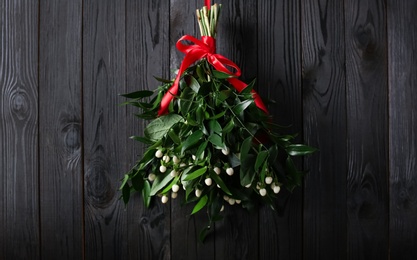 Photo of Mistletoe bunch with red bow hanging on dark wooden wall. Traditional Christmas decor