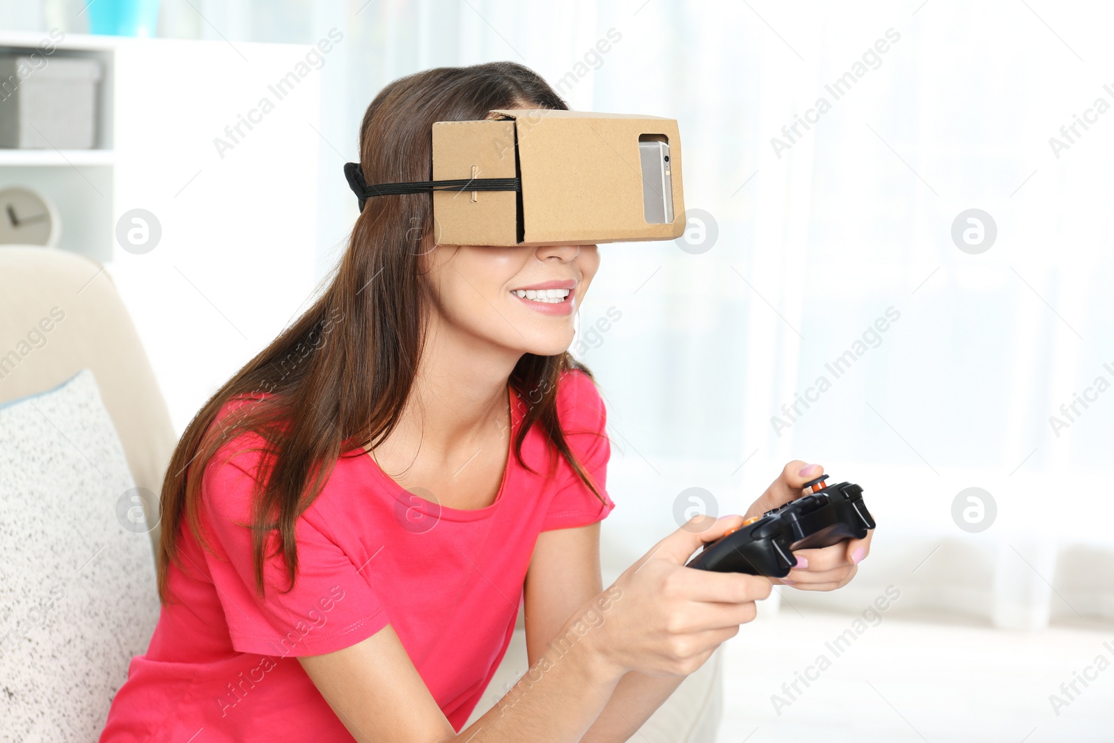 Photo of Young woman using cardboard virtual reality headset at home