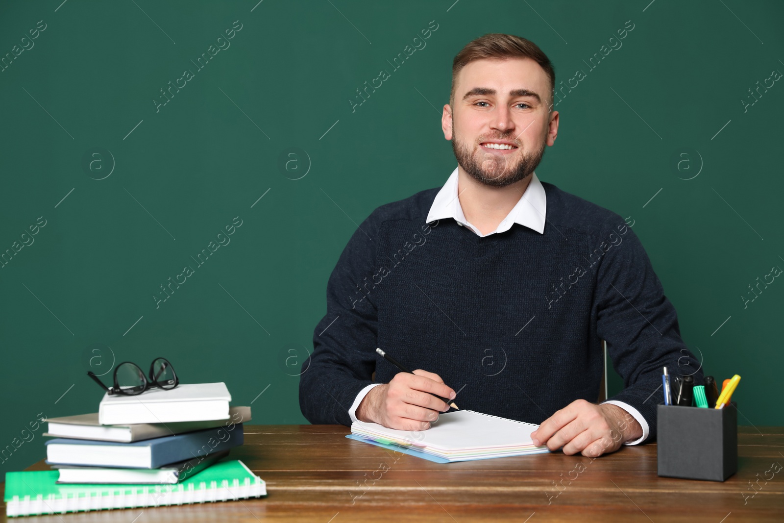 Photo of Portrait of young teacher at table against green background. Space for text