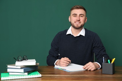 Portrait of young teacher at table against green background. Space for text