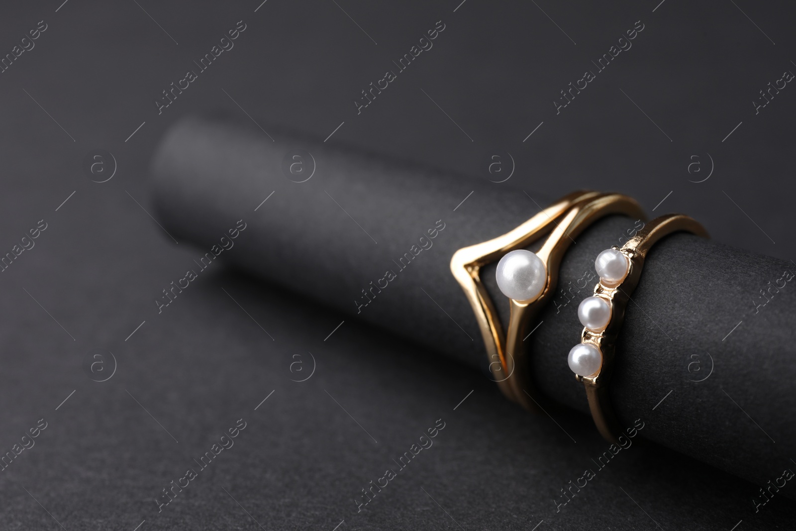 Photo of Elegant pearl rings on black background, closeup. Space for text