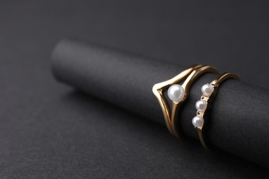 Photo of Elegant pearl rings on black background, closeup. Space for text