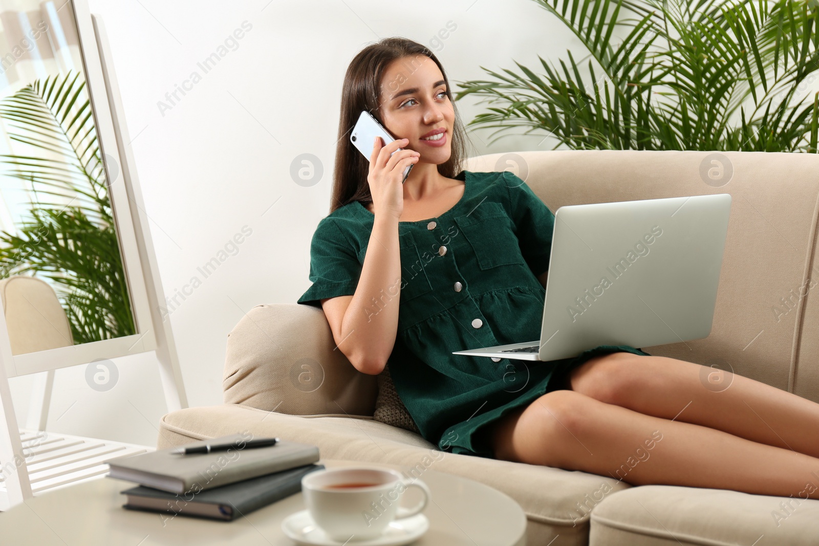 Photo of Young woman with laptop and mobile phone in living room. Home office concept