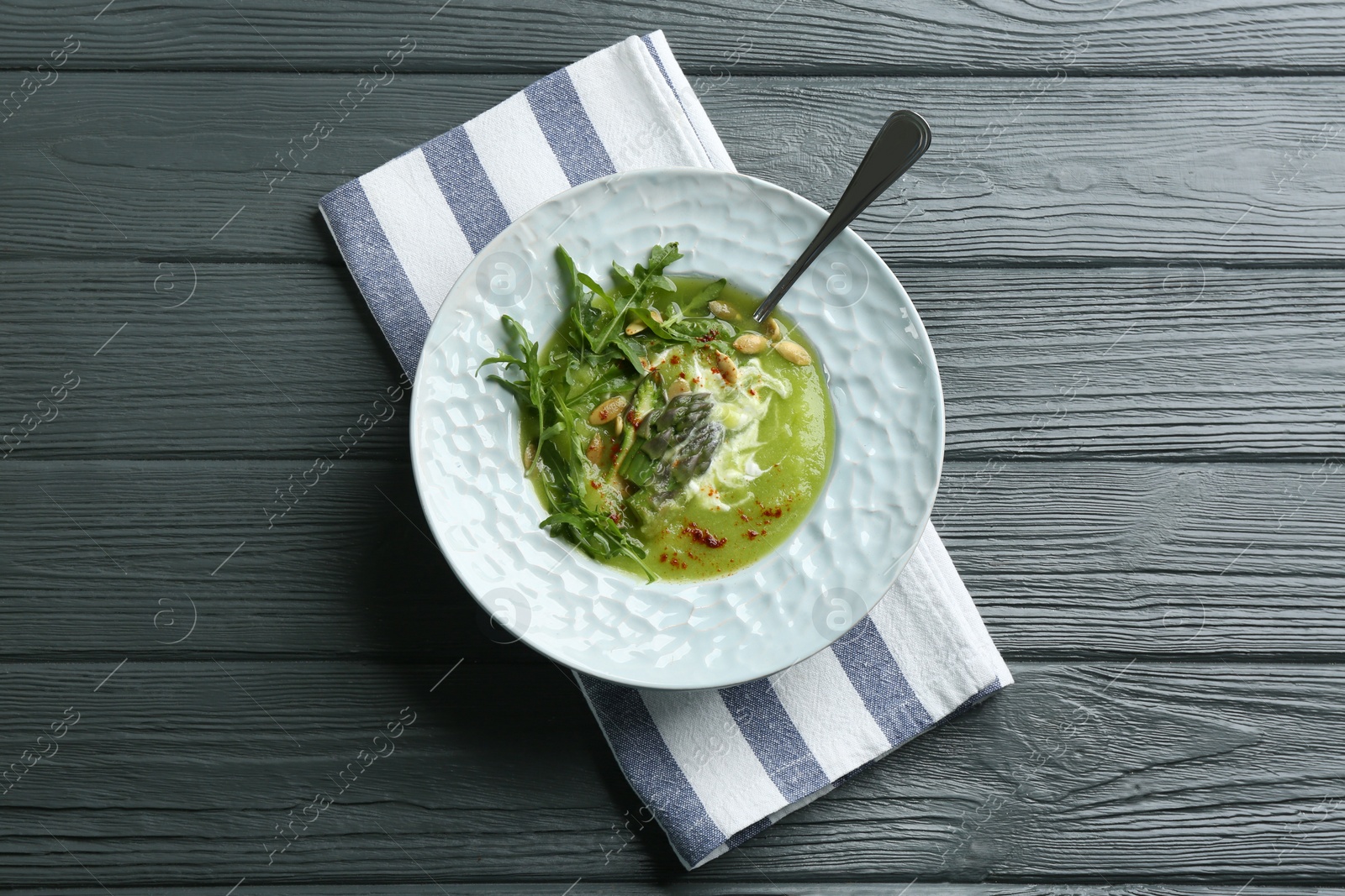 Photo of Delicious asparagus soup served on grey wooden table, top view