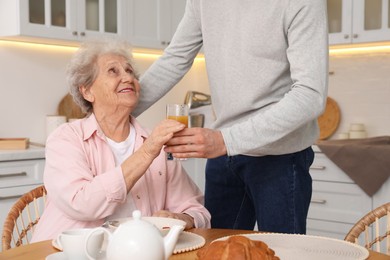 Photo of Young caregiver giving drink to senior woman in kitchen. Home care service