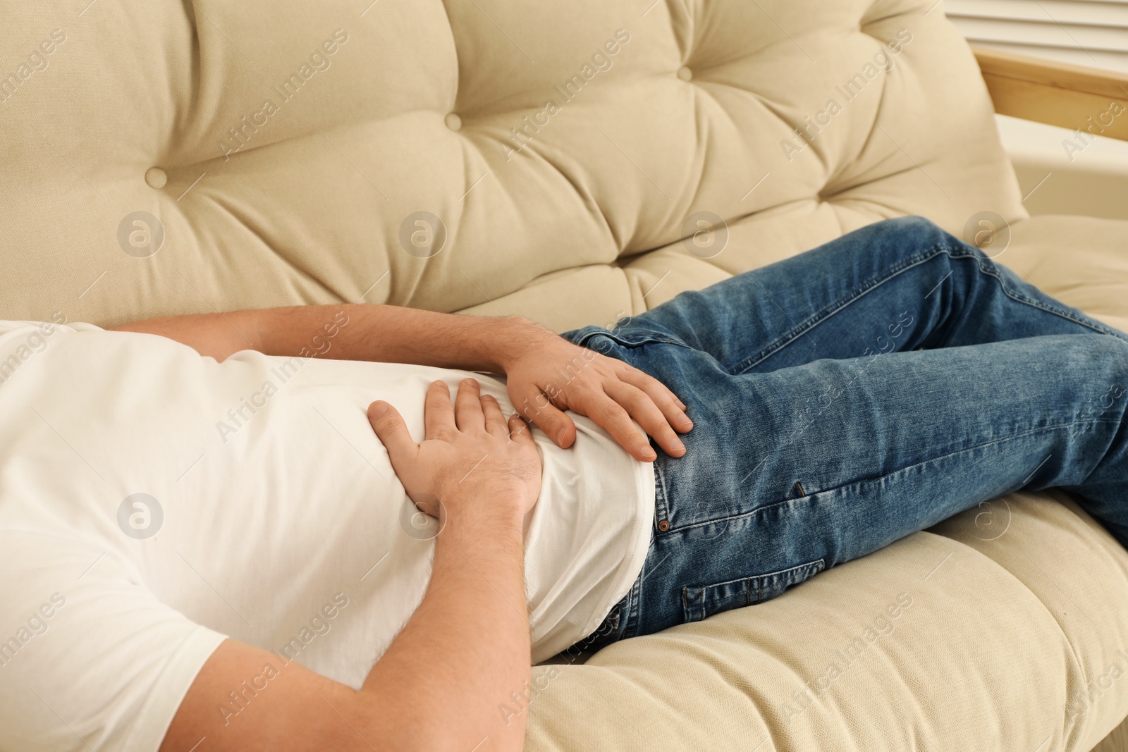 Photo of Man suffering from pain in lower right abdomen on sofa at home, closeup. Acute appendicitis