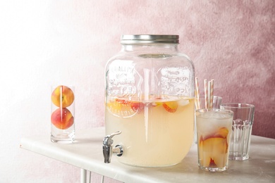 Photo of Peach cocktail in glass and jar with tap on table. Refreshing drink