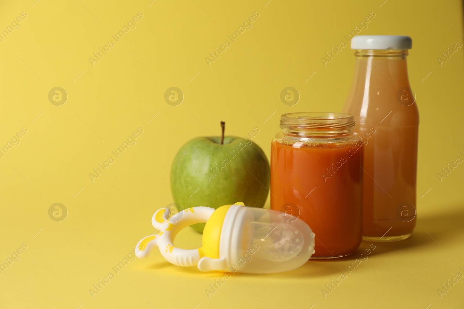 Photo of Healthy baby food, apple, juice and nibbler on yellow background, space for text