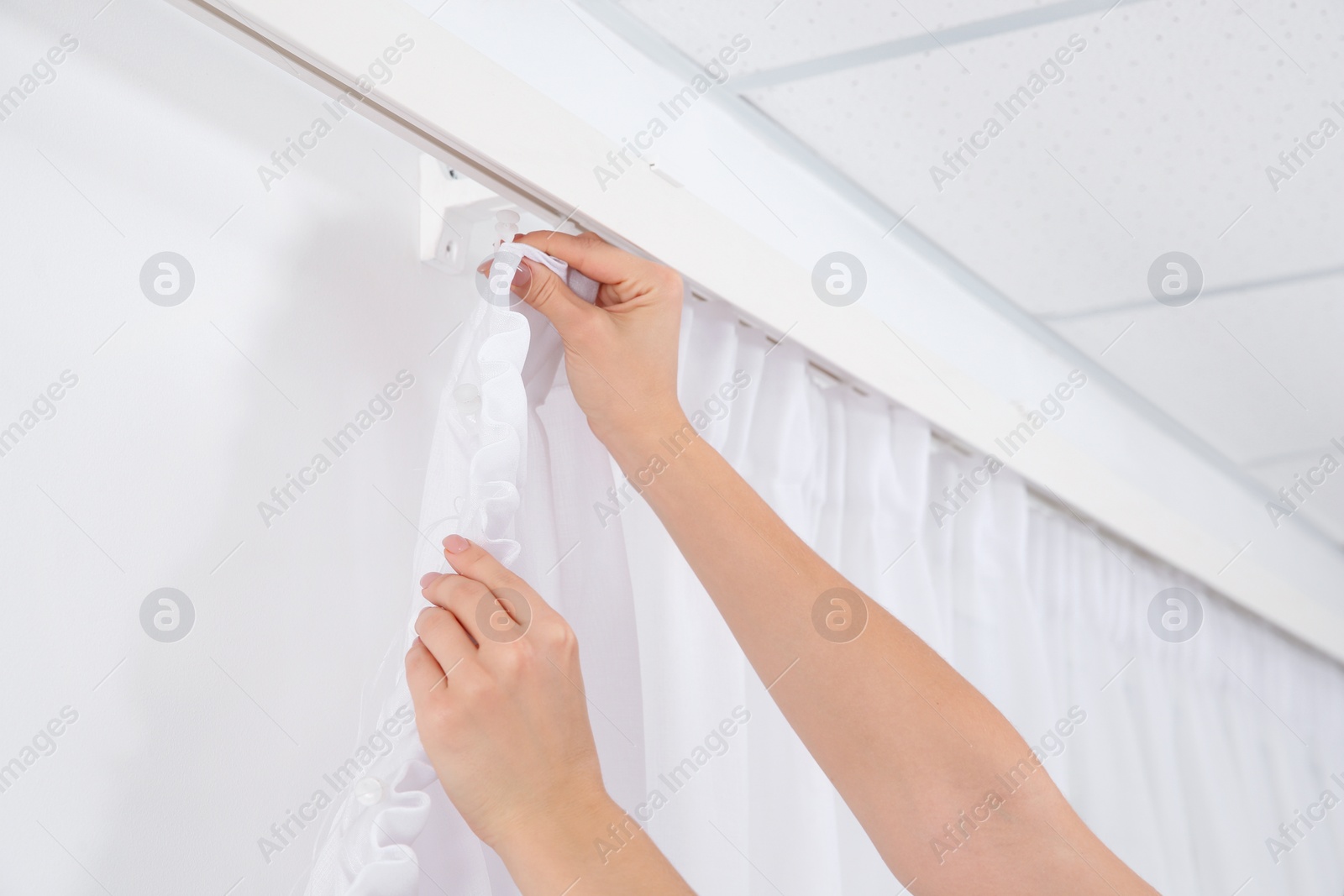 Photo of Woman hanging window curtain indoors, closeup. Interior decor element