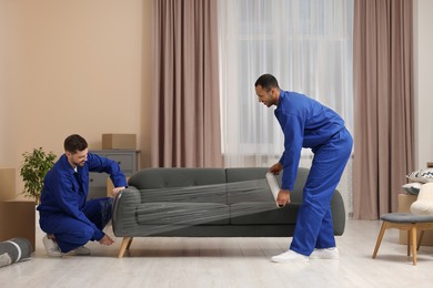 Photo of Male movers with stretch film wrapping sofa in new house