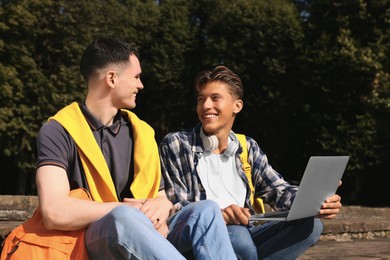 Photo of Happy young students studying with laptop together on steps in park