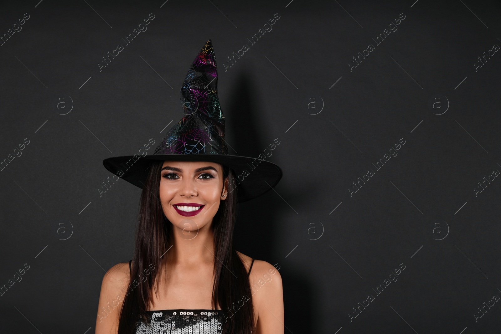 Photo of Beautiful woman wearing witch costume for Halloween party on black background, space for text