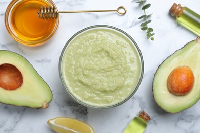 Homemade hair mask in bowl and ingredients on white marble table, flat lay