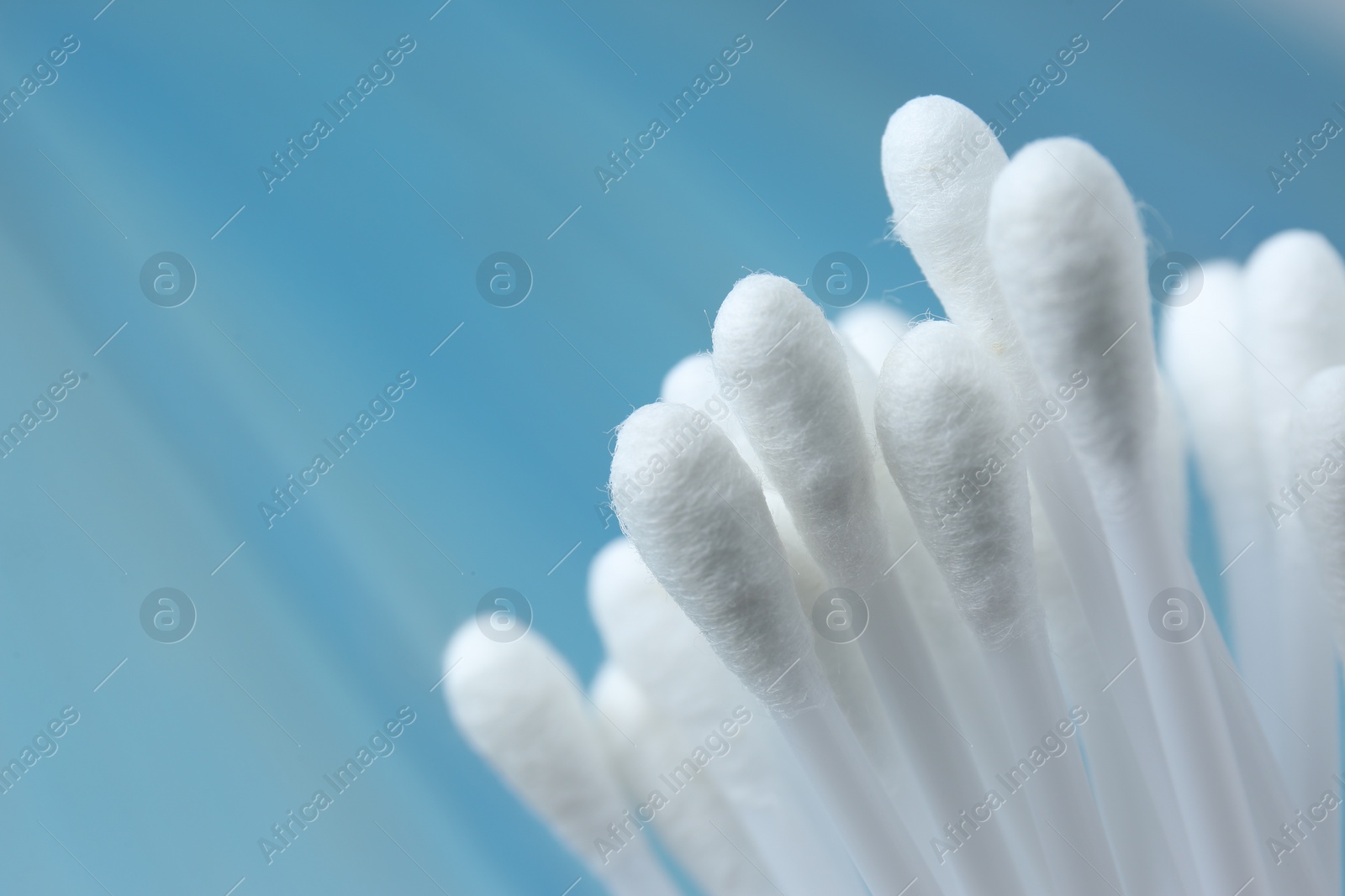Photo of Many cotton buds on light blue background, closeup. Space for text
