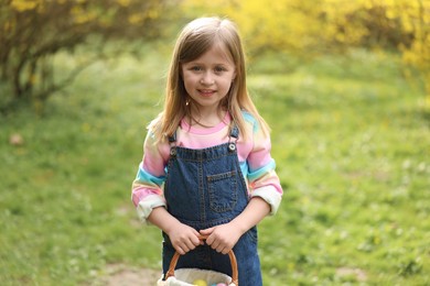 Easter celebration. Cute little girl holding wicker basket with painted eggs outdoors