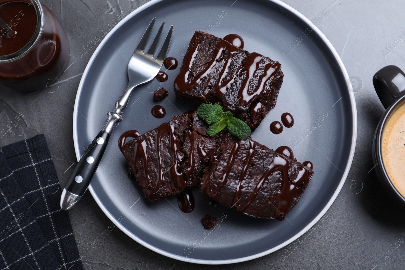 Photo of Delicious chocolate brownies with sweet syrup and mint served on grey table, flat lay