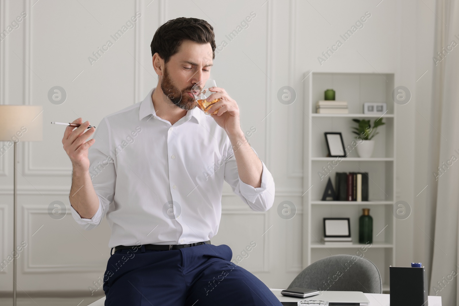 Photo of Man using cigarette holder for smoking and drinking whiskey in office