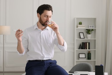 Photo of Man using cigarette holder for smoking and drinking whiskey in office