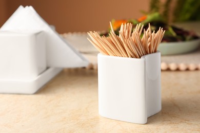 Photo of Holder with many toothpicks on beige table, closeup. Space for text