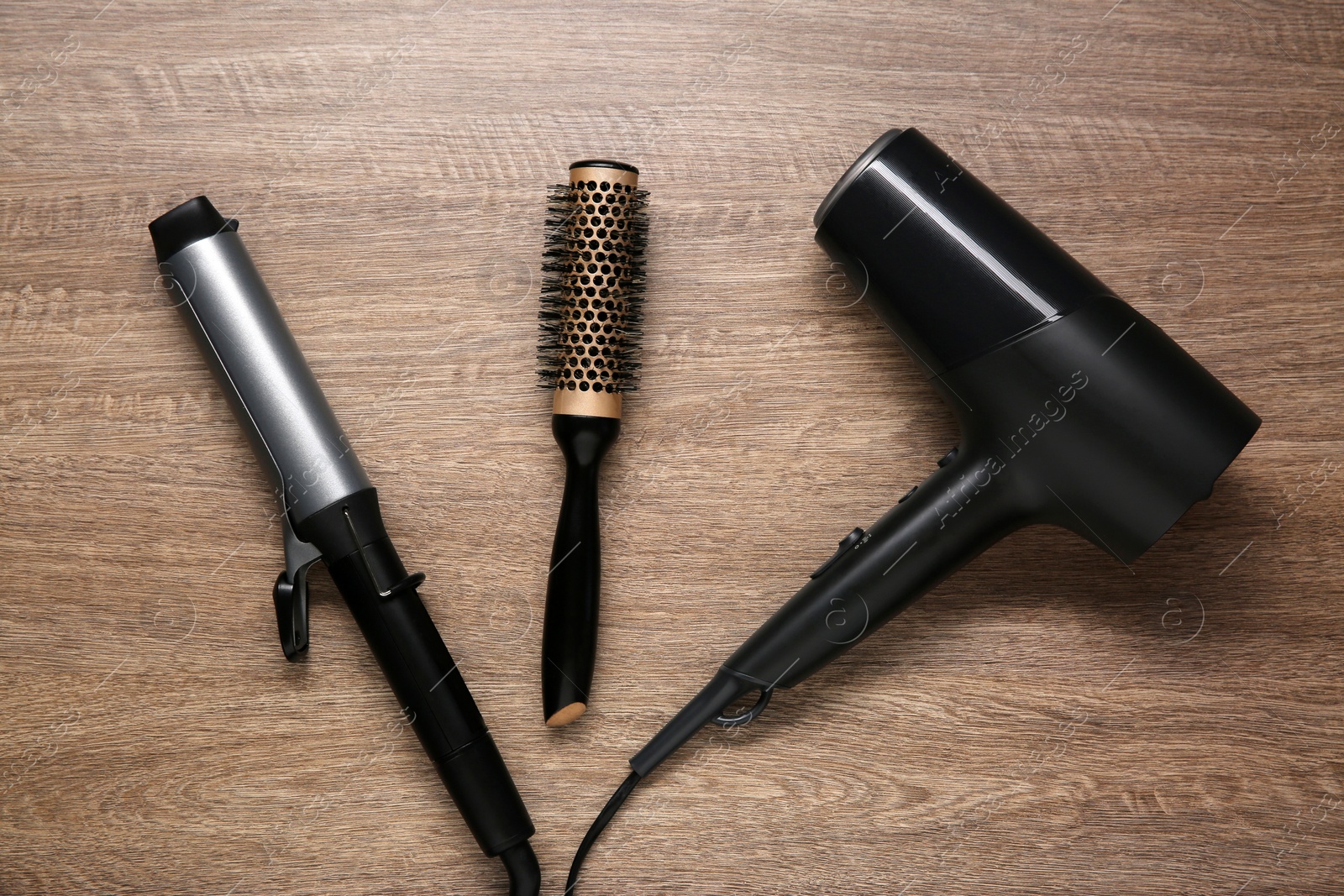 Photo of Curling iron, round brush and hair dryer on wooden background, flat lay