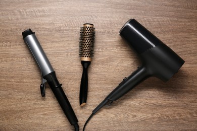 Curling iron, round brush and hair dryer on wooden background, flat lay