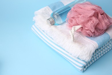 Photo of Pink shower puff, bottle of cosmetic product and towel on light blue background, space for text