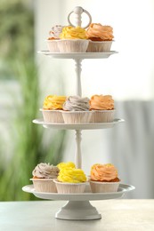 Photo of Dessert stand with tasty cupcakes on white table indoors, closeup