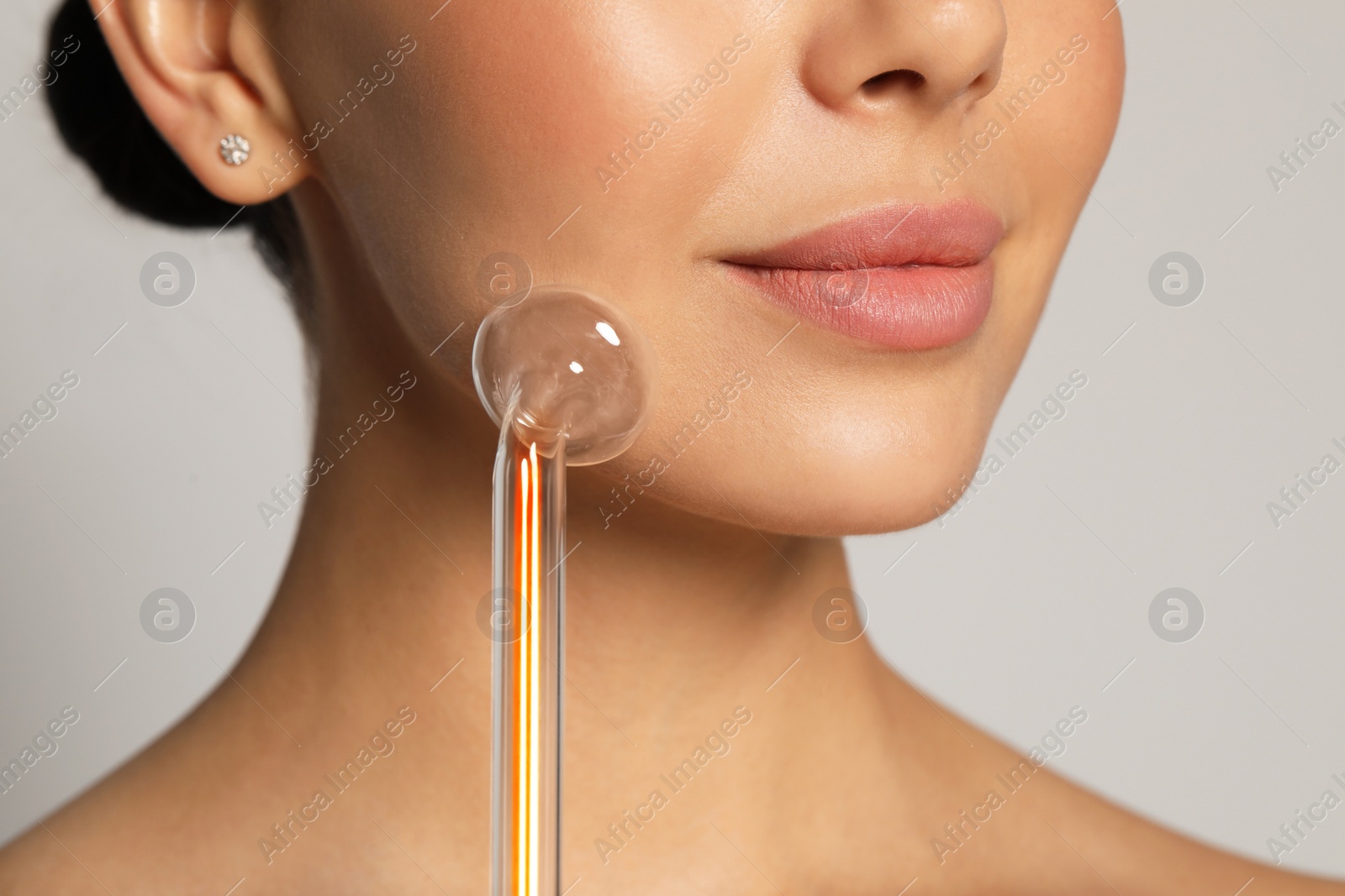 Photo of Woman using high frequency darsonval device on grey background, closeup