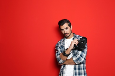 Young photographer with professional camera on red background. Space for text