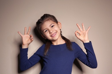 Photo of Little girl showing OK gesture in sign language on color background