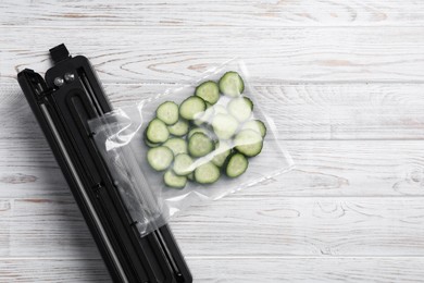 Photo of Vacuum packing sealer with plastic bag of cucumbers on white wooden table, flat lay. Space for text