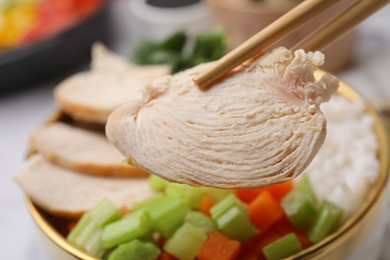 Photo of Chopsticks with piece of chicken above poke bowl, closeup